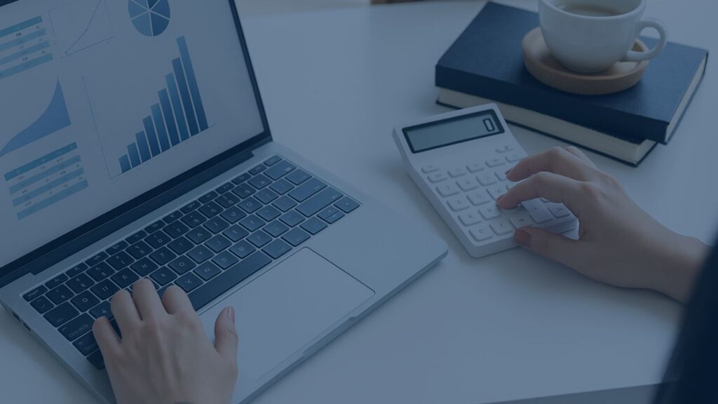 laptop showing a dashboard of graphs and hand typing on a calculator