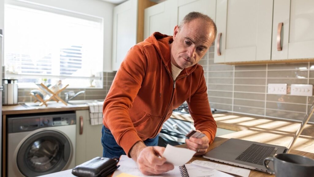 man stood in kitchen holding a bill