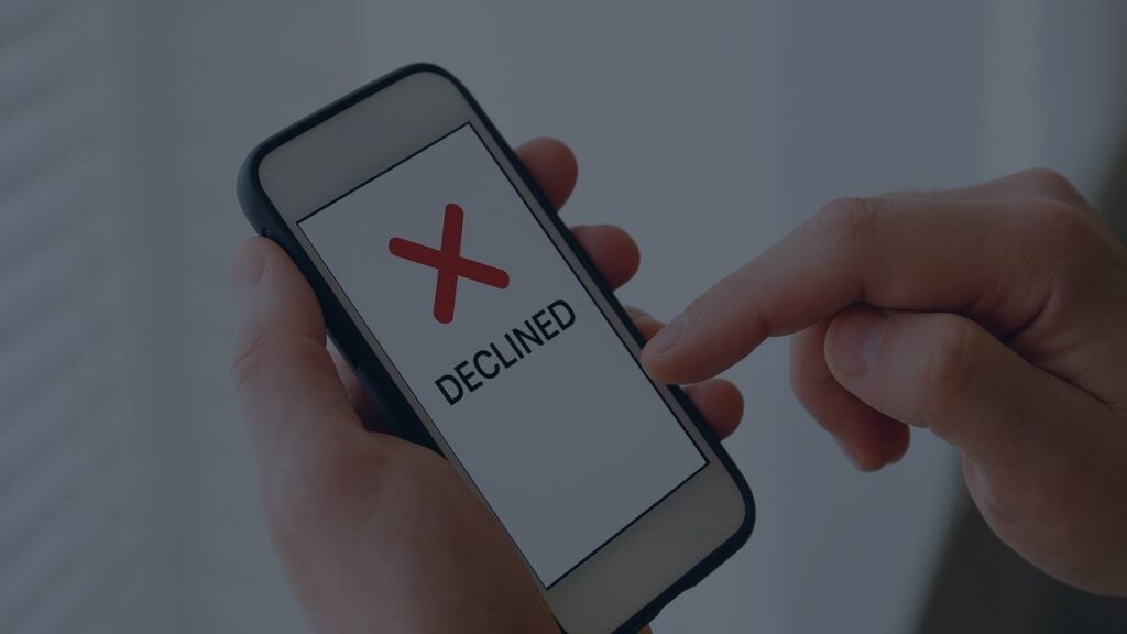 person holding mobile phone with a red cross and text saying declined credit on screen