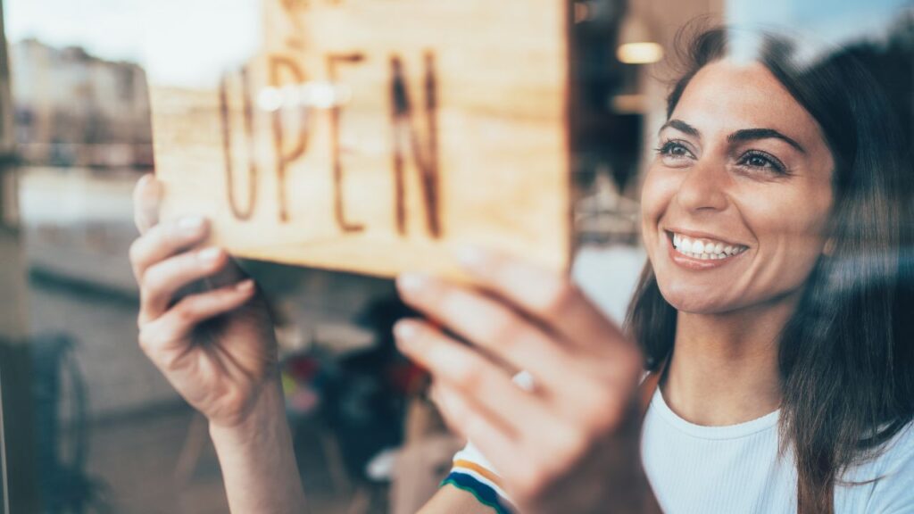 Small business owner smiling while hanging an open sign in a shop window